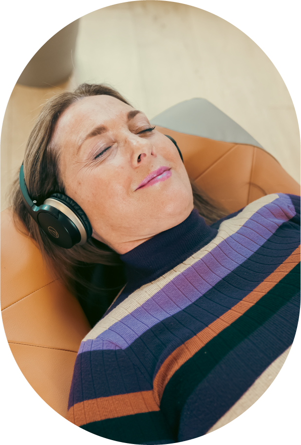 A smiling woman laying on the BackHug device with headphones